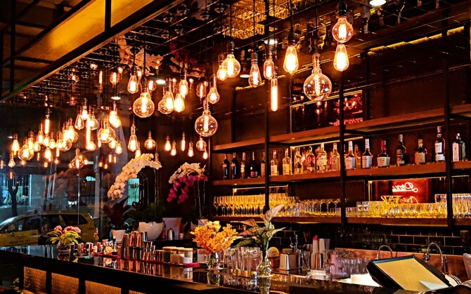 a rustic-looking bar brightly-lit with Edison bulbs of many different sizes and shapes