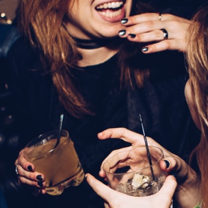 two women holding rock glasses talking to each other